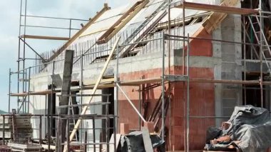 İşçiler inşaat sahasında, açık bir günde iskele ve malzemelerle yeni bir iskan binası inşa etmekle meşguller. İlerleme devam ettikçe heyecan artıyor.