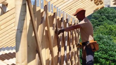 Kendini işine adamış bir işçi, ahşap kirişleri titizlikle bir yapı için birleştirir, açık gökyüzünün altında yemyeşil bir zemin arasında sanatını sergiler..