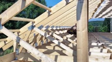 İnşaat işçileri, parlak ve güneşli bir kırsal bölgede kereste kirişlerinden yapılmış çatı iskeletini birleştiriyorlar. Arka planda güzel ağaçlar var..