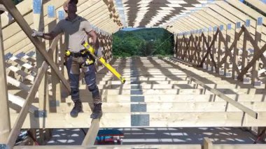 İşçiler uzak bir ortamda ahşap bir çerçeve inşa ediyorlar, açık gökyüzü ve bol güneş ışığı altında takım çalışması ve işçiliği sergiliyorlar..