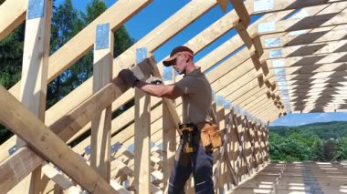 Yetenekli bir işçi titizlikle ahşap kirişleri dış mekan manzaralı bir çatıya yerleştirir, kendini adamışlık ve zanaatkarlık sergiler..