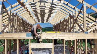 Bir müteahhit gün boyunca açık gökyüzünün altında manzaralı bir alanda bir yapı için ahşap iskelet oluşturmaya çalışır..
