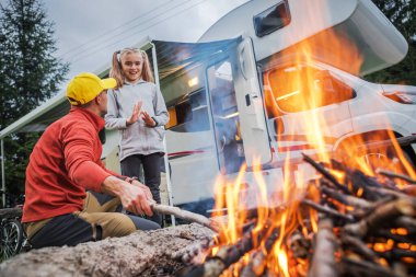 Bir adam ve bir kız kamp yerindeki karavanın dışındaki kamp ateşinde gülüp kaynaşıyorlar. Atmosfer hayat dolu, yaz maceraları için mükemmel..