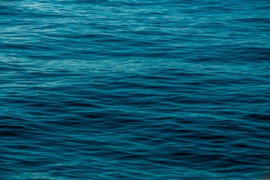 Turkuaz suyun sakin yüzeyi sıcak öğleden sonra ışığı altında hafif dalgalar sergiliyor ve dinlenmek için ideal sakin bir atmosfer yaratıyor..