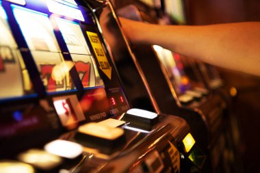 Canlı bir kumarhanede kumar makinesiyle etkileşime geçen bir oyuncu renkli ışıklar ve sesler arasında heyecanlı bir oyun akşamının tadını çıkarıyor..