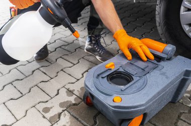 Eldivenli bir kişi açık bir günde park yerinde araba yıkamak için tuvalet kaseti ve çözelti hazırlıyor..