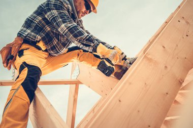 İnşaat alanında ahşap kirişleri korumaya odaklanmış bir inşaat işçisi. Koruyucu giysiler giyiyor, görev sırasında yeteneklerini ve hassasiyetini gösteriyor..