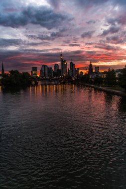 Güneş Frankfurt 'un ufuk çizgisinin arkasında batarken gökyüzünü canlı bulutlar kaplıyor. Aşağıdaki nehri yansıtıyor ve çarpıcı bir akşam atmosferi yaratıyor..