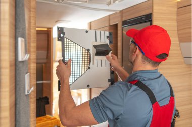 Kırmızı şapkalı bir teknisyen dikkatle yeni bir hava filtresini şık bir karavanın içine yerleştiriyor..