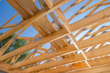 Bir çatı yapısı için ahşap kirişler monte ediliyor, parlak mavi gökyüzüne karşı ayrıntılı işçilik sergileniyor, devam etmekte olan bir inşaat projesini vurguluyorlar.