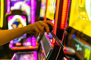 Bir oyuncu renkli bir kumarhanede kumar makinesine bağlanıyor, neon ışıklar bölgeyi aydınlatıyor, geceleri heyecan verici ve canlı bir atmosfer yaratıyor..