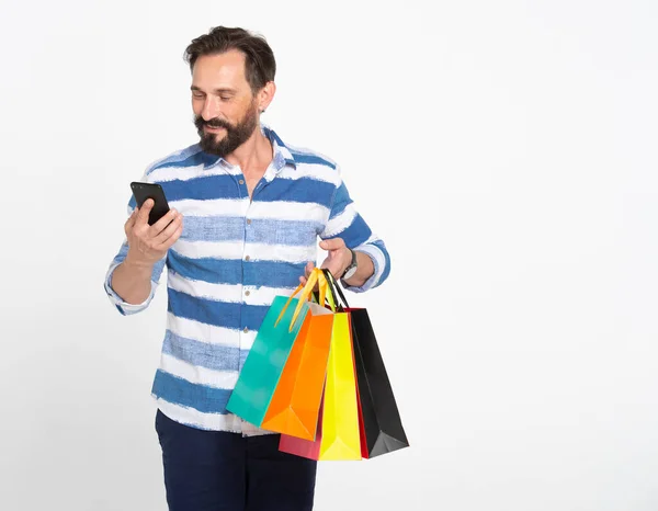 Homem Barba Atraente Olhando Para Segurando Smartphone Monte Sacos Compras — Fotografia de Stock