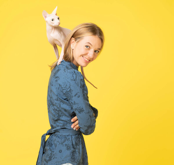Beautiful woman with a sphynx cat on back. profile side view portrait of nice-looking attractive lovable fascinating magnificent winsome cheerful young woman isolated over yellow background