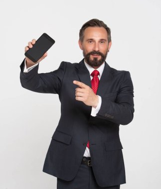 Mavi takım elbiseli, beyaz gömlekli, kırmızı kravatlı, akıllı telefon siyah ekranını işaret eden ve elinde cep telefonu olan mutlu çekici iş adamı.
