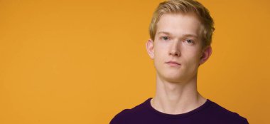 Turuncu arka planda izole edilmiş çekici sarışın bir adamın portresi.