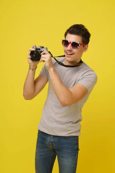 Güneş gözlüklü neşeli genç adam ellerinde fotoğraf makinesi ile izole edilmiş bir resim çekiyor.