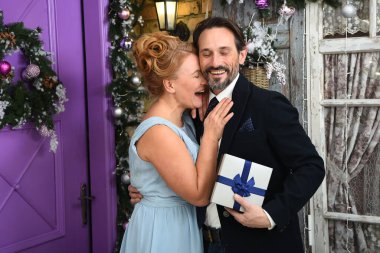 Happy elinde hediye kutusu olan adama yaslandı. Mor kapılı ve Noel süslemeleri takan mavi elbiseli çekici orta yaşlı kadın. Hediye kutusunu tutan adam
