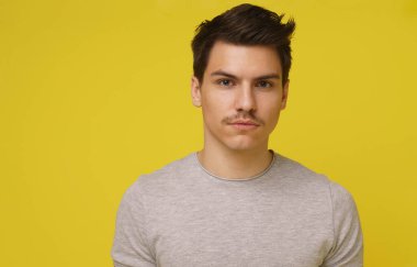 20 'li yaşlarda, bıyıklı, sarı arka planda izole edilmiş kameraya bakan çekici bir adamın fotoğrafı..