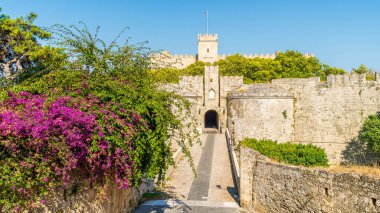 Rodos 'taki Amboise Kapısı, tarihi turizm için mükemmel taş kale duvarları ve canlı çiçeklerle ortaçağ mimarisi ve doğal güzelliğinin çarpıcı bir karışımını sergiliyor..