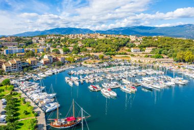 Korsika 'daki Porto-Vecchio marinasının hava manzarasında lüks yatlar, yelkenliler ve dağlar ve Akdeniz tarafından çerçevelenmiş manzaralı bir kıyı köyü yer alıyor..