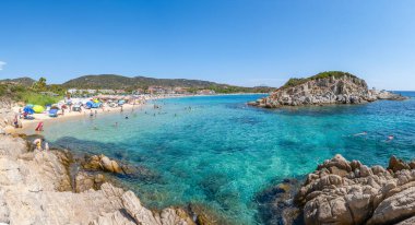 Sithonia, Yunanistan - 2 Eylül 2025: Yunanistan 'ın Sithonia kentindeki Kalamitsi Sahili, turkuaz sular, altın kum, plaj şemsiyeleri, kayalık adalar ve geleneksel bir sahil köyü ile.