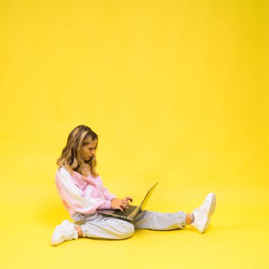 Beautiful little girl sitting on light floor with a gray laptop and smiling, empty space