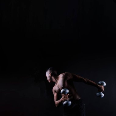 Isolated african muscular man with dumbbells on a dark studio background. Strong shirtless black guy