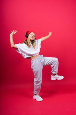 Girl listening to music in headphones on a red background. Cute child enjoying dance music, smile