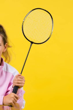 Full length studio photo of ten year old girl holding a badminton racket and isolated on yellow.