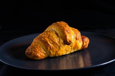 Yeni desteklenmiş Fransız kruvasanı güneş ışınlarında parlıyor, karanlık arka plan, mutfak.