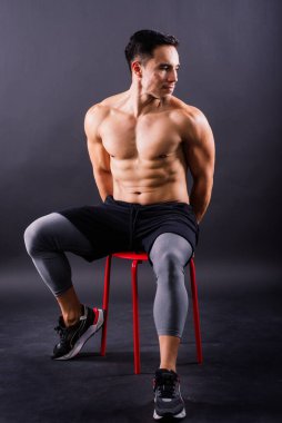 Kaslı, üstsüz, kendinden emin genç bir adam. Önden, kameraya bakıyor.