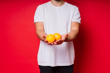 Kırmızı arka planda portakalla poz veren yakışıklı bir gencin stüdyo portresi.