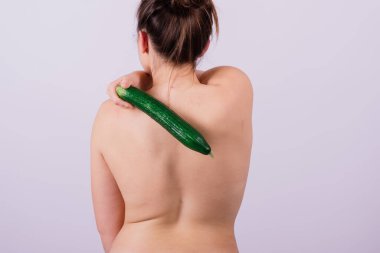 Beyaz arka planda salatalıkla soyutlanmış üstsüz bir kadın cesedi.