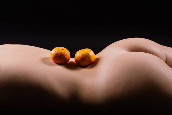 Апельсины, мандарины - цитрусовые на женском теле. Голая женщина лежит на спине с фруктами, расположенными