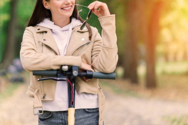 Sonbahar parkında elektrikli scooter kullanan genç bir kadın. Yeşil ulaşım, trafik sıkışıklığı.