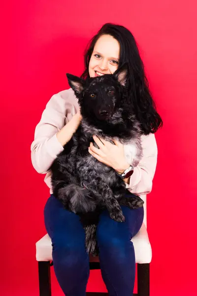Happy brunette lady in a casual wear hugging mudi pet dog, studio background.