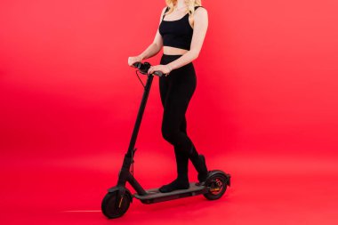 Kırmızı ve beyaz arka planda sarışın bir kadın oturur ve elektro scooter ile durur ve dinlenir.