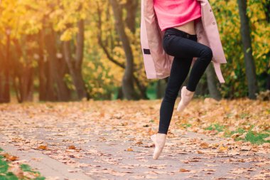 Altın sonbahar parkında sivri ayakkabılarla dans eden kadın balerin, sarı yaprakların üzerinde bale pozu veriyor.