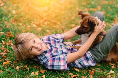 Çocuk sonbaharda bir köpeğe sarılıyor ve onunla kırıştırıyor, şehir parkında