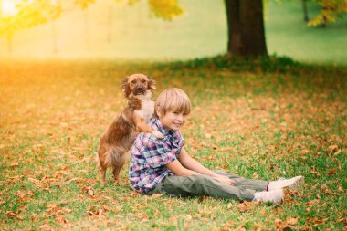Çocuk sonbaharda bir köpeğe sarılıyor ve onunla kırıştırıyor, şehir parkında