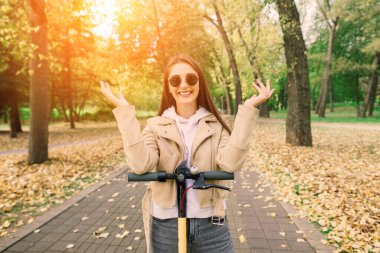 Güz parkında elektrikli scooter süren güzel bir kadın, ekolojik nakliye.