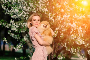 Çekici genç bir kadın köpek salyası tutuyor ve kameraya gülümsüyor, parkta yürüyor. İnsanlar ve hayvanlar arasındaki dostluk kavramı.