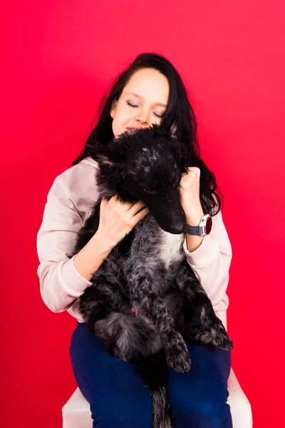 Happy lady in a casual wear hugging purebred pet dog, mudi with owner over studio background.