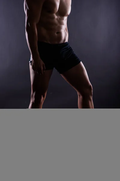 Muscular male legs, man in a studio, dark background