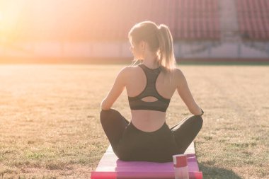 Genç bir bayan stadyumda yoga yapıyor.