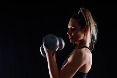 Spor kıyafetli atletik bir kadın dambıl kaldırıyor sağlıklı bir hayat sürüyor mutlu bir ifadesi var.