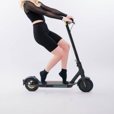Spor elbiseli bir kadın, kırmızı ve beyaz arka planda güneş gözlüklü elektrikli scooter 'ın üzerinde duruyor.