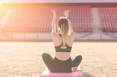 Genç bir bayan stadyumda yoga yapıyor.