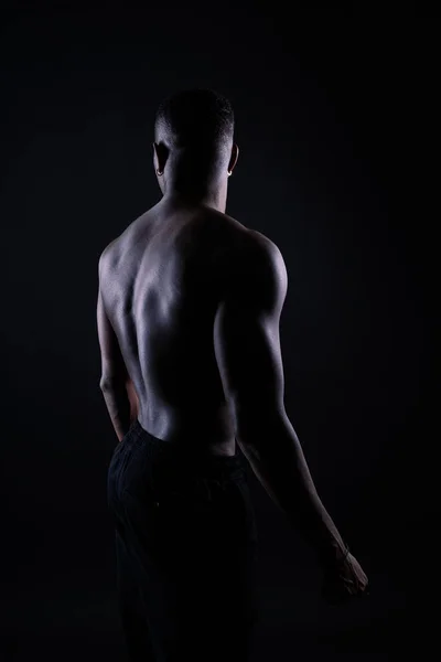 One young african muscular build man standing topless silhouette isolated on a black background