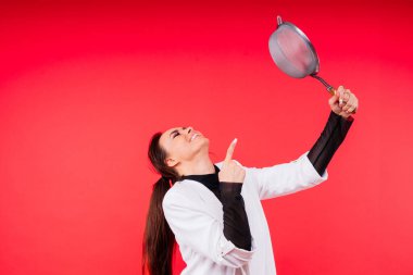 Mutlu genç sarışın kadın stüdyodaki kırmızı beyaz bsckground 'da elekten geçirir.